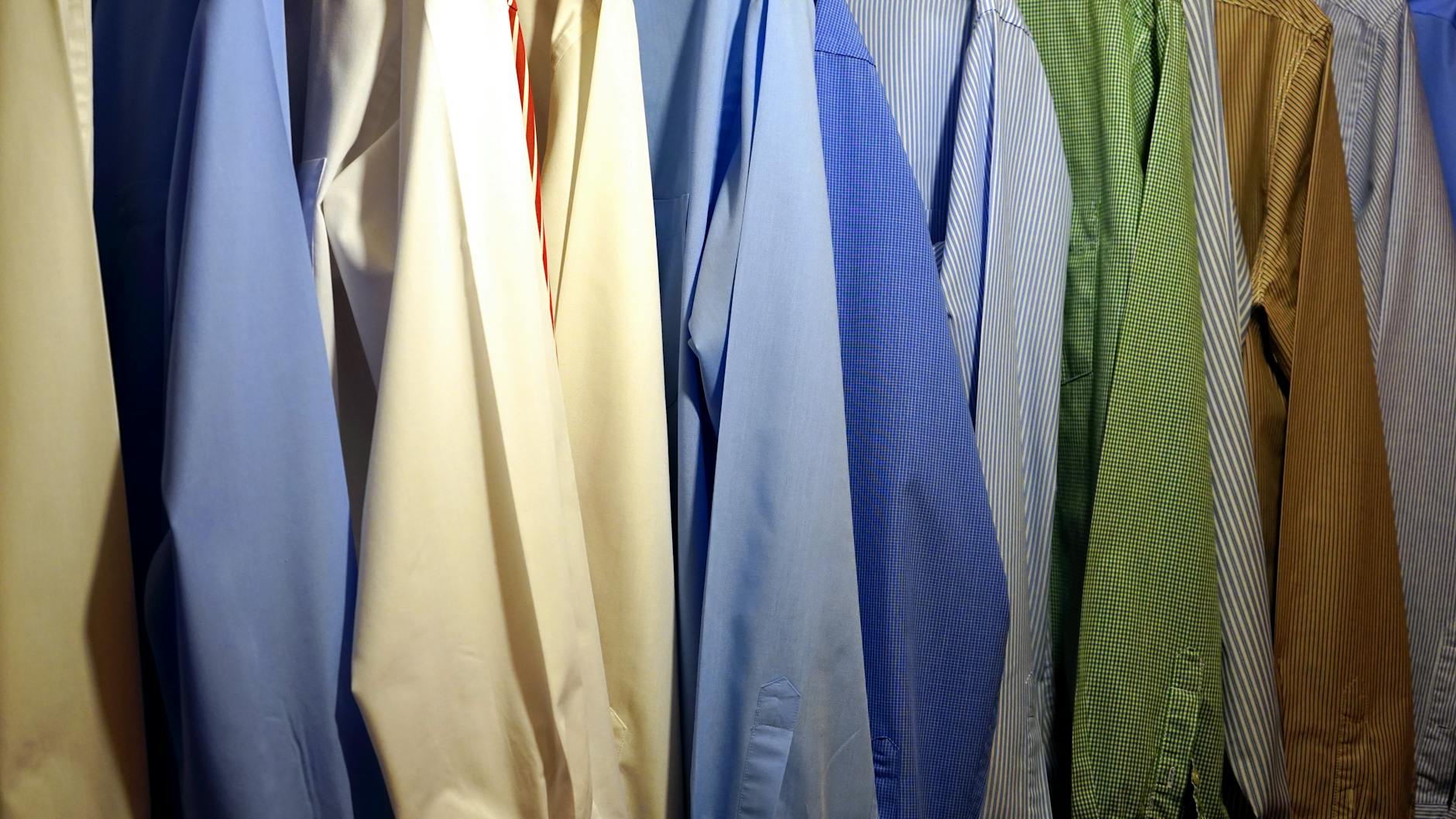 A collection of colorful dress shirts hanging in a row, featuring various shades including blue, green, yellow, and striped patterns.